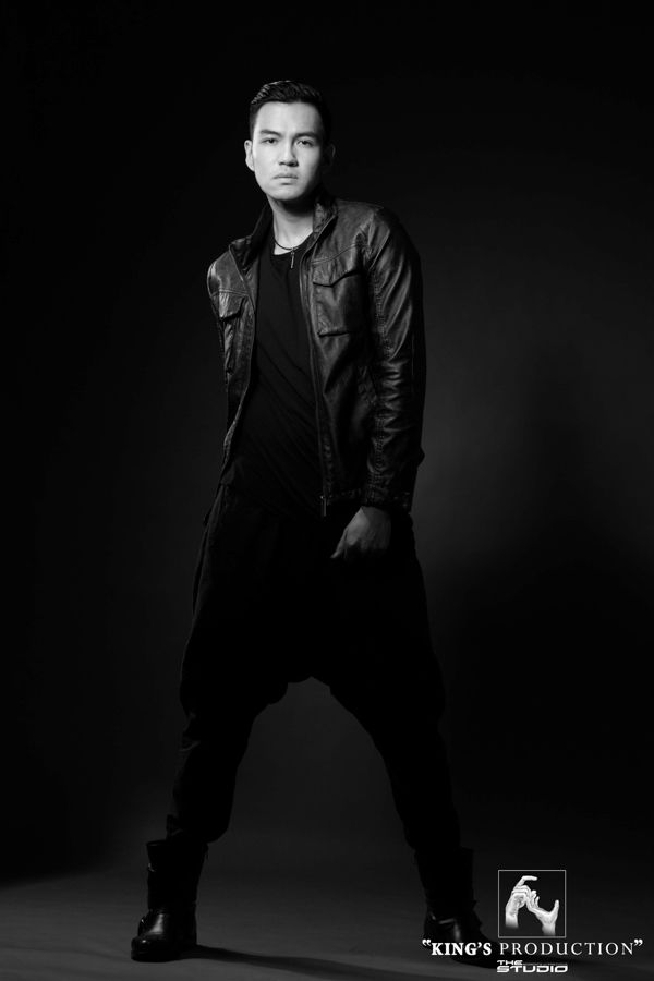 身穿全黑服裝、皮夾克、深色背景、時尚姿勢的男子。