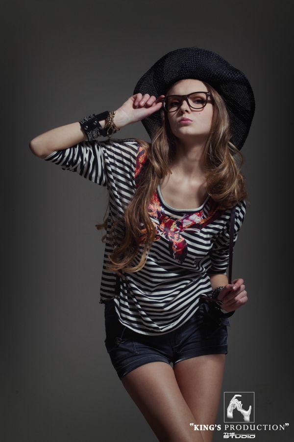 戴著帽子、眼鏡、穿著條紋襯衫和短褲的女人在工作室裡擺姿勢。