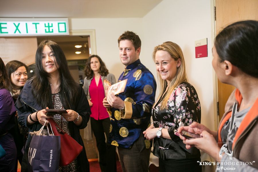 出口附近，一群人面帶微笑，交談著。一位身穿藍金色夾克的男子手裡拿著一份禮物。