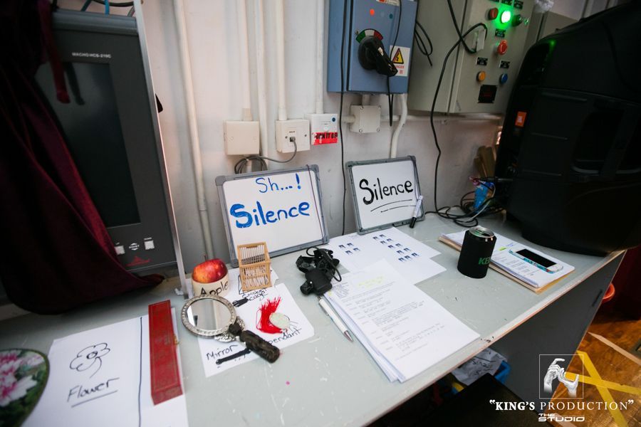 一張凌亂的桌子上，放著寫著「安靜」和「噓！安靜」的標語。桌上還有各種物品，包括紙張和放大鏡。