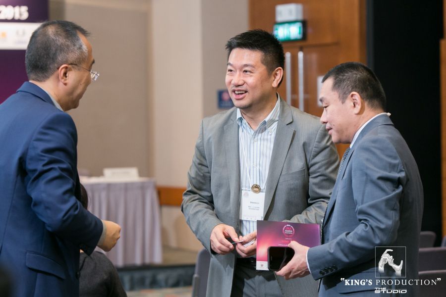 三位西裝革履的男士在會議上交談；其中一人手裡拿著一本小冊子，背景為中性色。