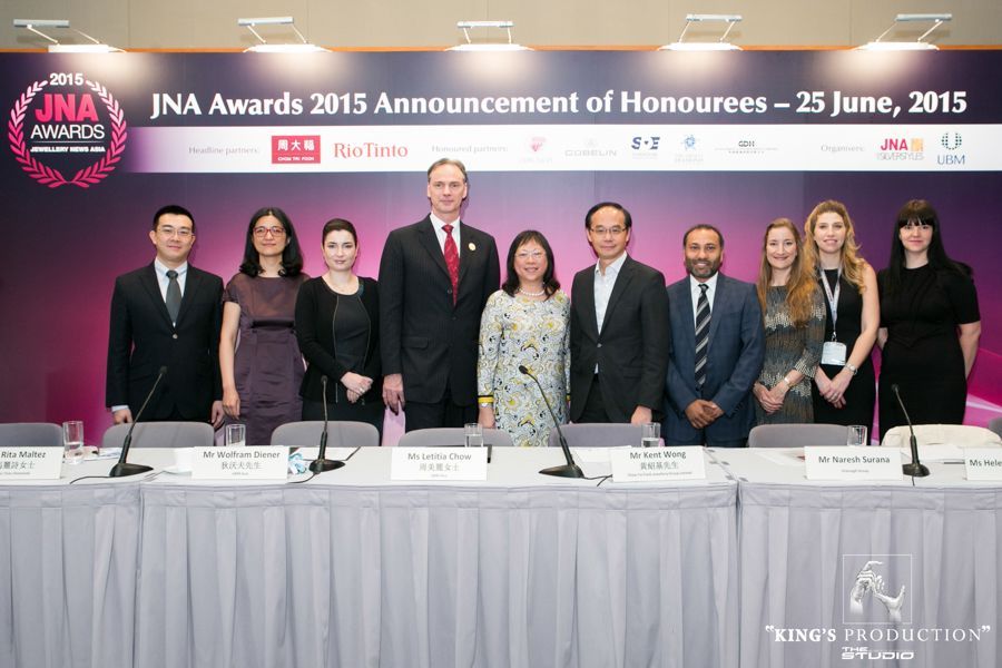 2015年度JNA大獎頒獎典禮現場，一群人站在桌子後面。背景為紫色。