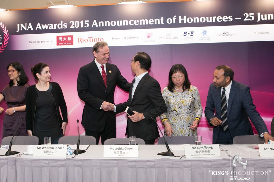 在JNA大獎頒獎典禮上，人們握手。一位西裝革履的男士與另一位西裝革履的男士握手；其他人在一旁觀看。