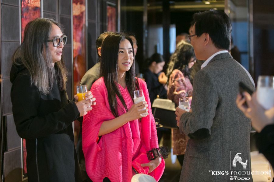 人們在室內聚會社交，其中包括一名身穿粉紅色衣服、手拿飲料的女子。