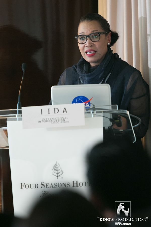 一位女士在四季酒店的講台上發表演講，筆記型電腦上貼著「IIDA」和 NASA 的貼紙。