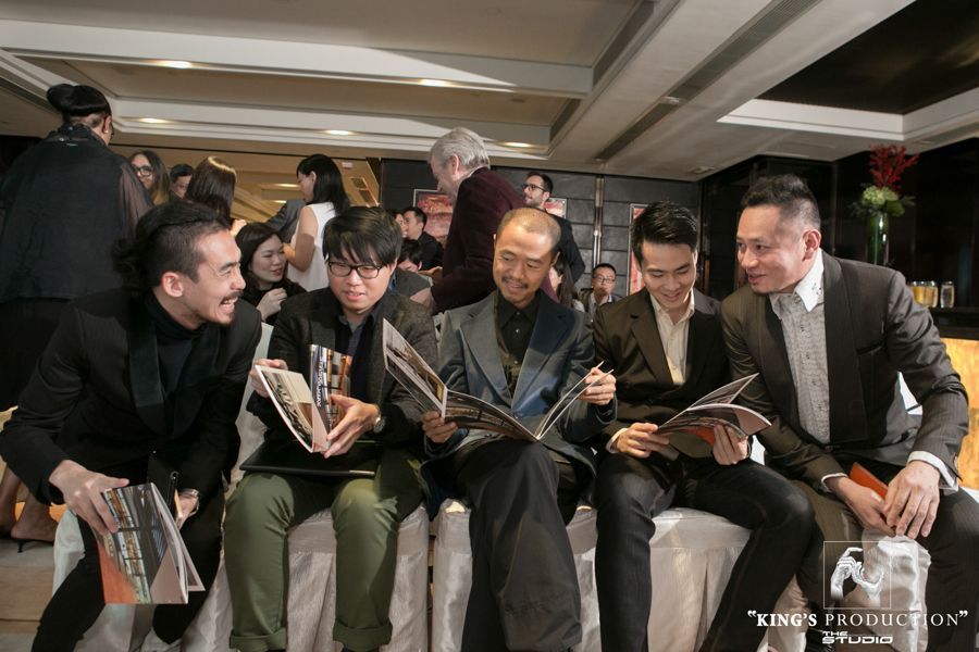 一群男子正在閱讀小冊子，可能是在某個活動上。他們坐著，西裝革履，面帶微笑。