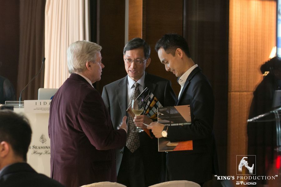 活動中，三位西裝革履的男士，其中一人手持一本書，手裡拿著酒杯討論。