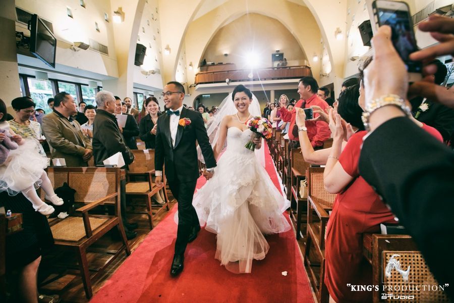 新婚夫婦微笑著走過走道，客人們歡呼並拍照，教堂內部。