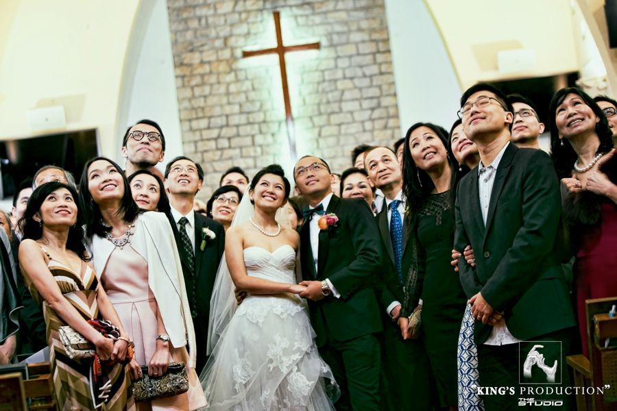 教堂裡的婚禮團體仰望十字架，有新娘、新郎和微笑的賓客。