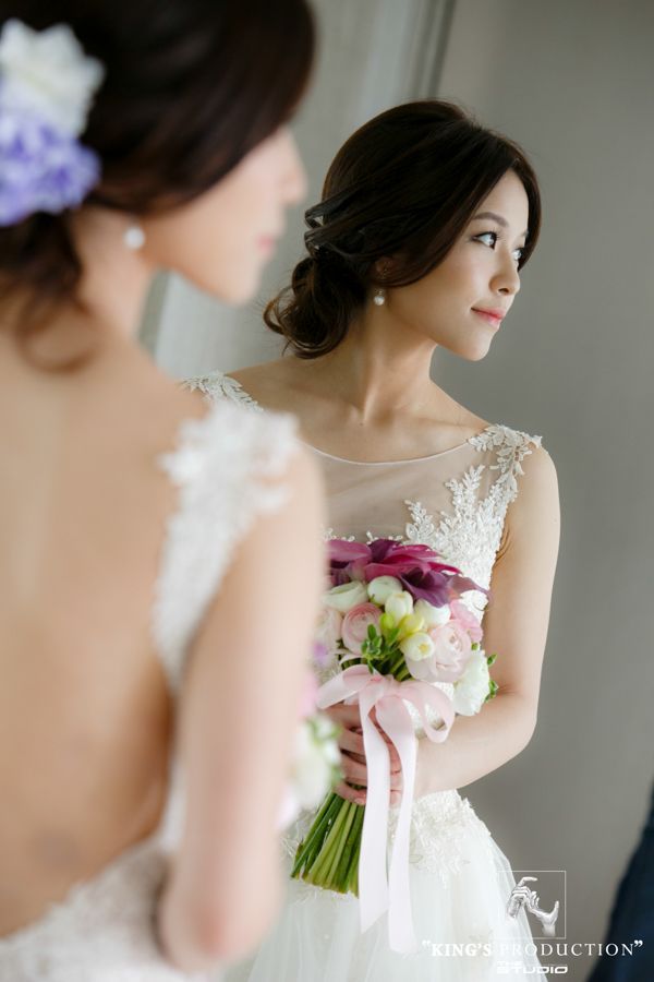 新娘穿著婚紗，手捧花束，看著鏡子中的自己。