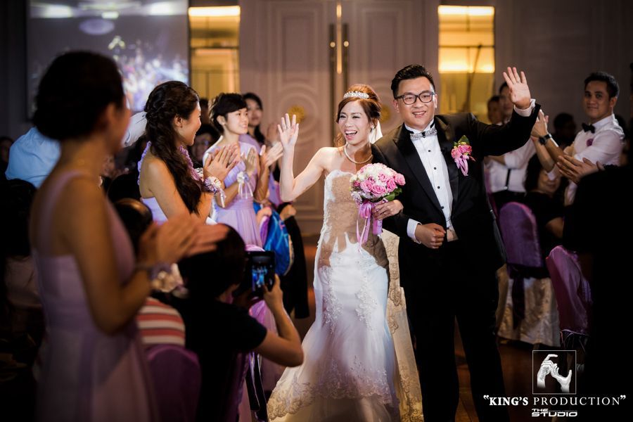 新郎新娘揮手致意，穿過房間，賓客們掌聲不斷。他們正在參加一場婚宴。