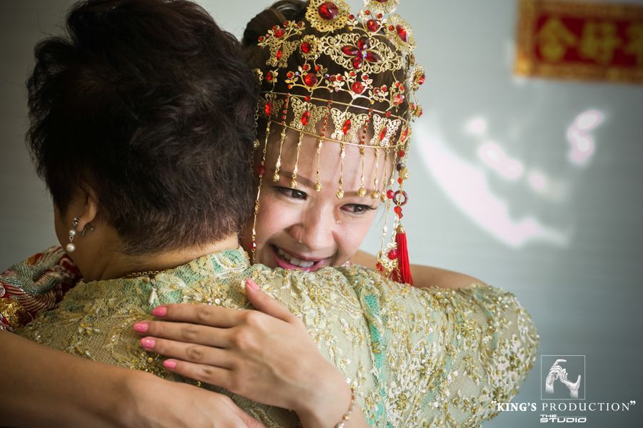 在明亮的房間裡，戴著傳統金色頭飾的新娘擁抱著年長的女士，兩人都面帶微笑。