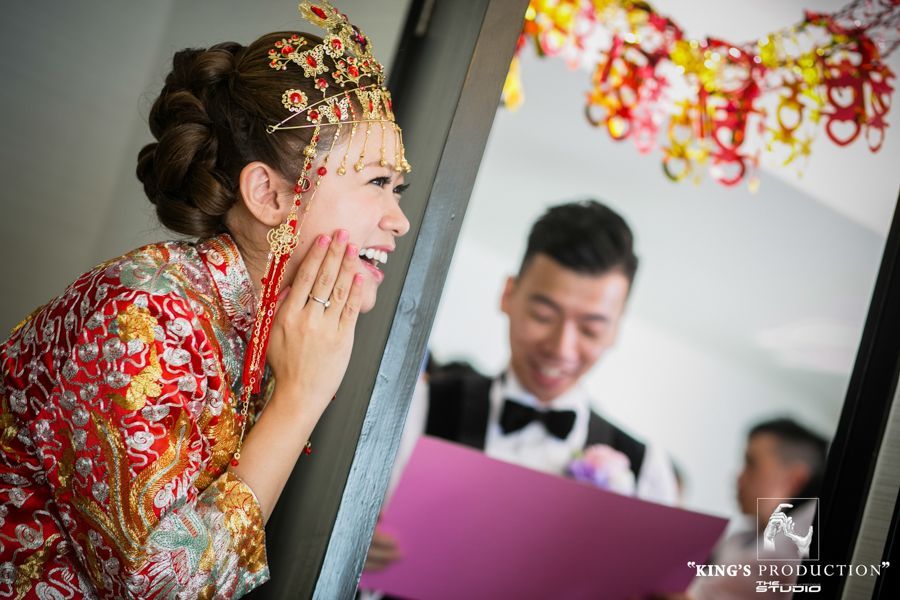 身穿傳統紅色和金色服裝的新娘笑了，看著拿著粉紅色卡片的新郎。
