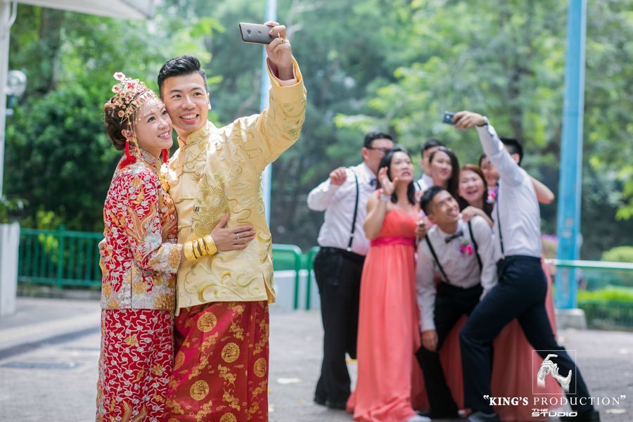 身穿傳統婚禮服裝的新娘和新郎與一群朋友在戶外自拍。