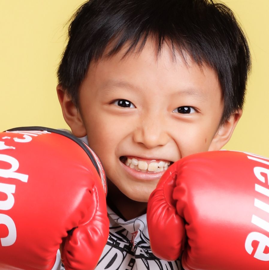 黃色背景下，戴著紅色拳擊手套、笑容燦爛的小男孩。