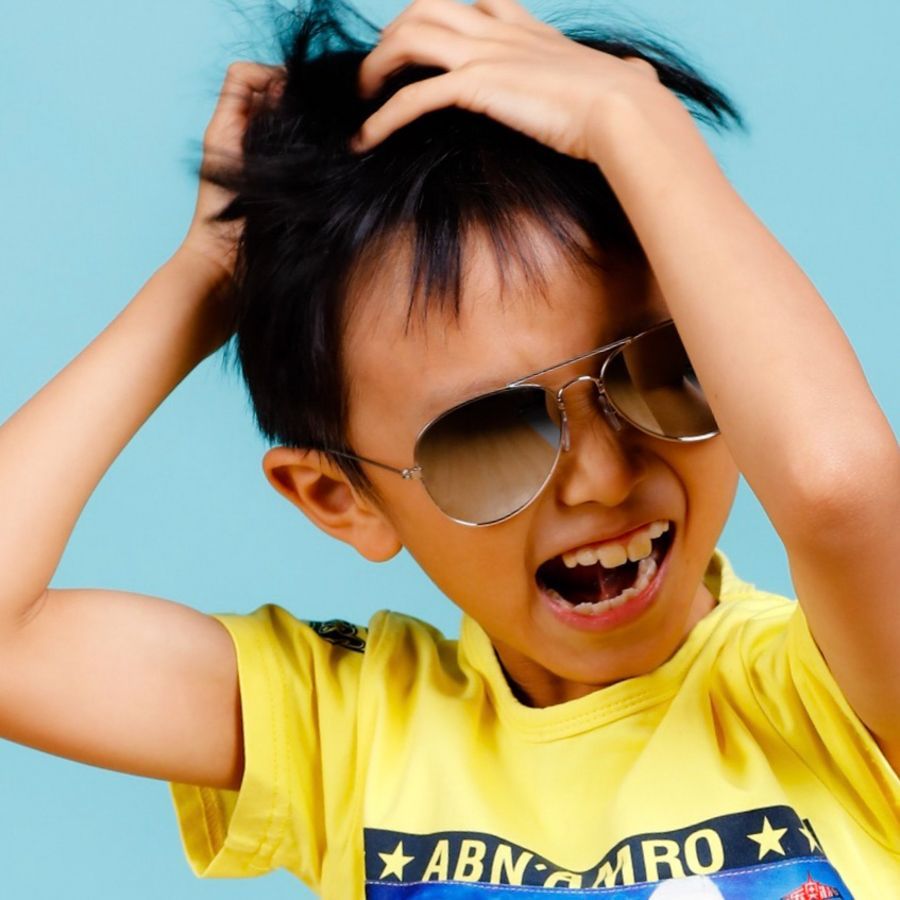 戴著太陽眼鏡的男孩在藍色背景下穿著黃色襯衫，大喊大叫，拉扯頭髮。