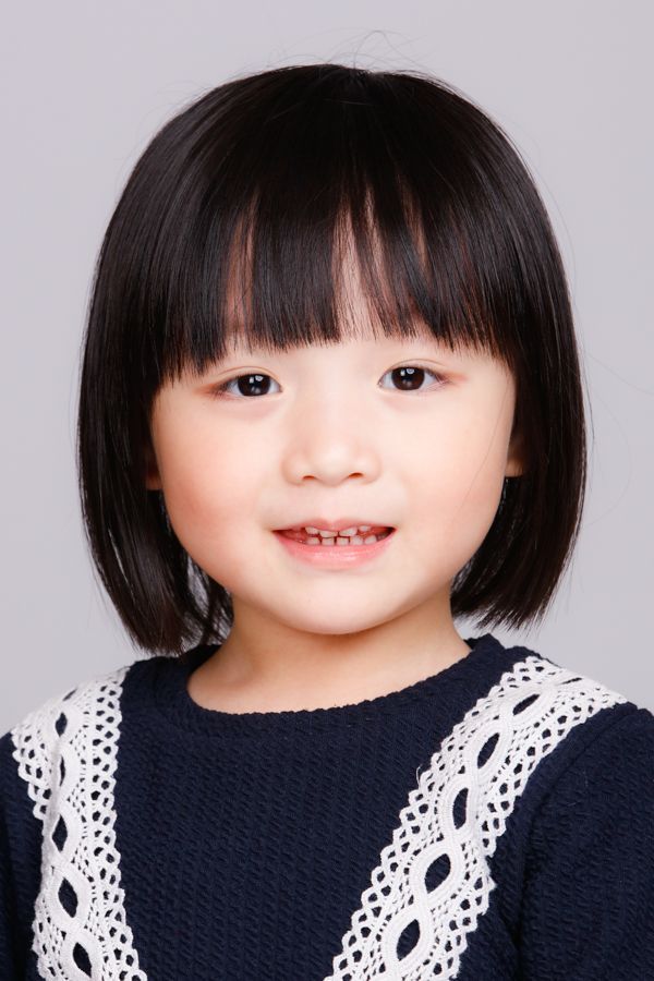 年輕的亞洲女孩，有著深色頭髮和瀏海，面帶微笑，穿著帶有白色蕾絲邊的海軍藍毛衣。