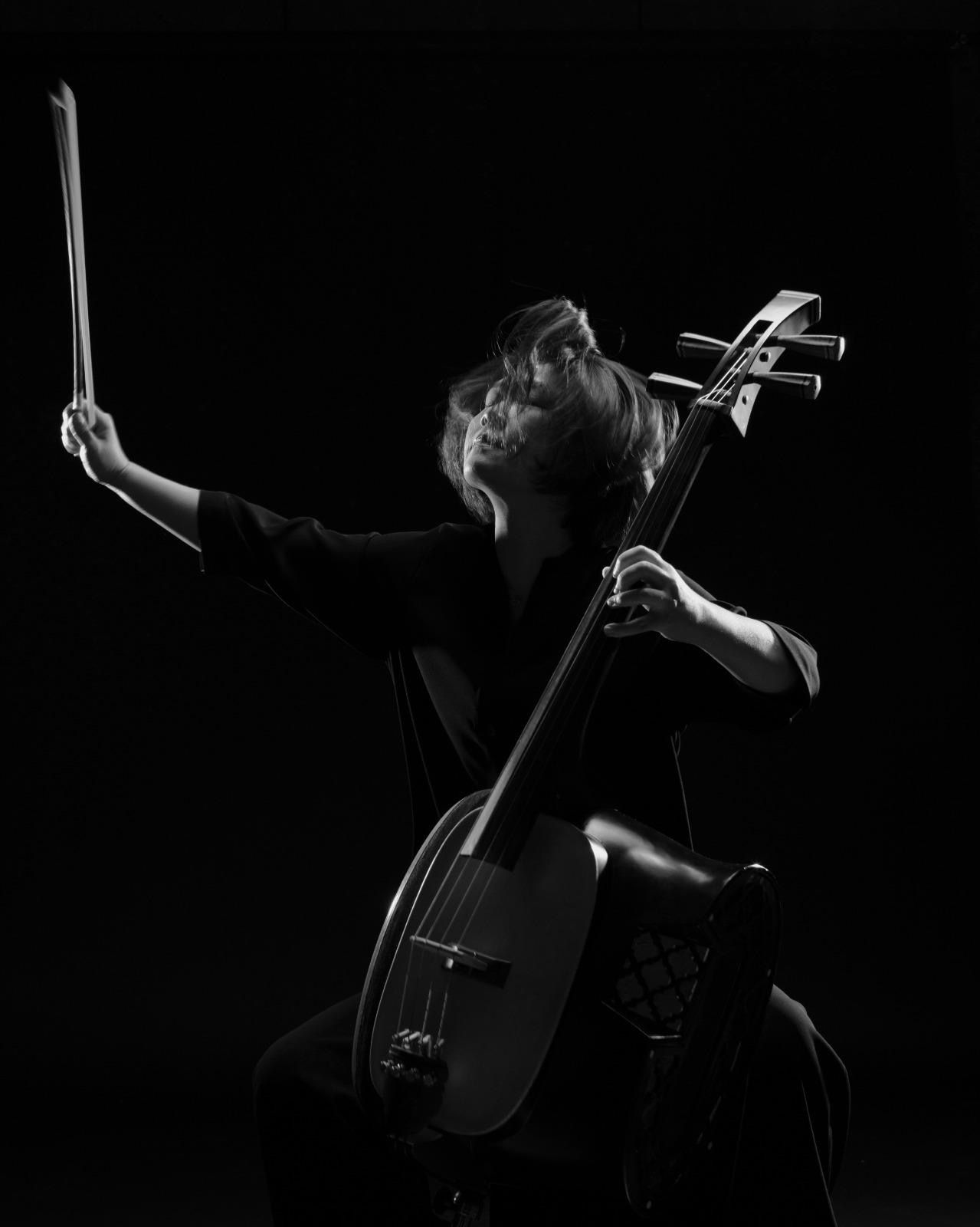 音樂家在黑色背景下演奏琵琶（一種亞洲琵琶），燈光明亮而富有戲劇性。