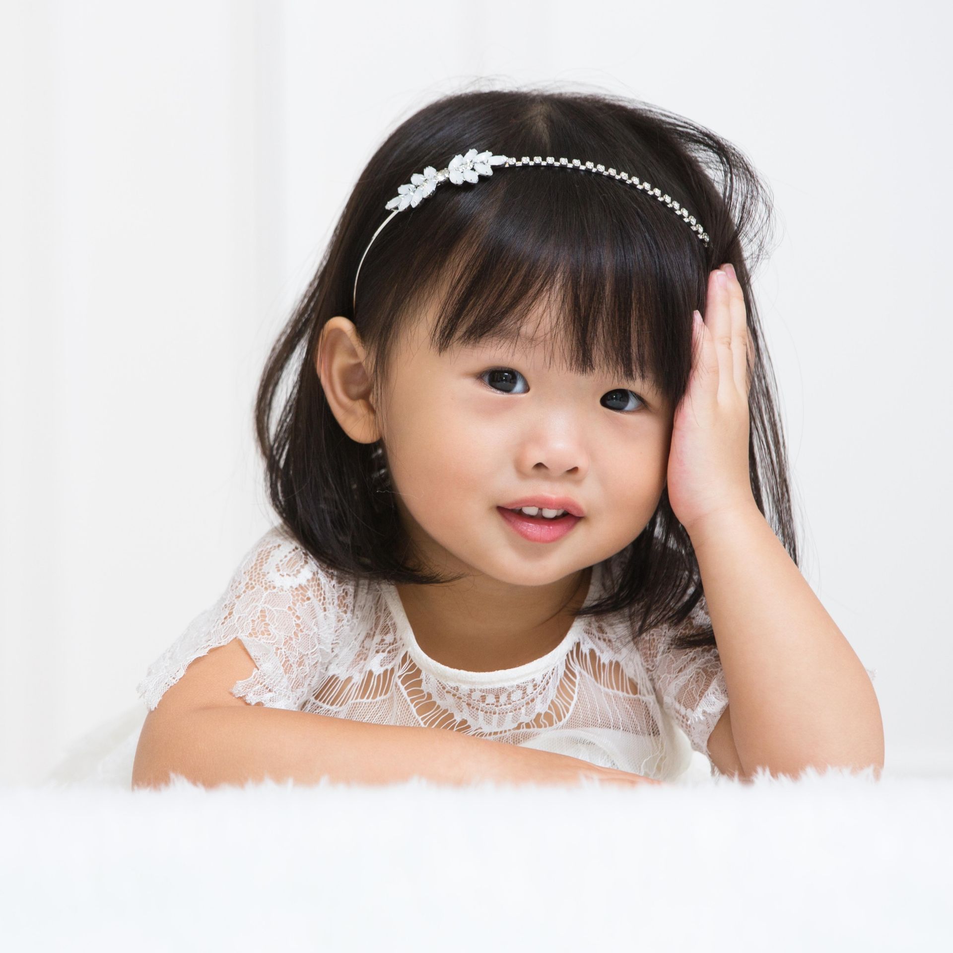 戴著頭帶的亞洲年輕女孩，用手托著頭，對著鏡頭微笑。