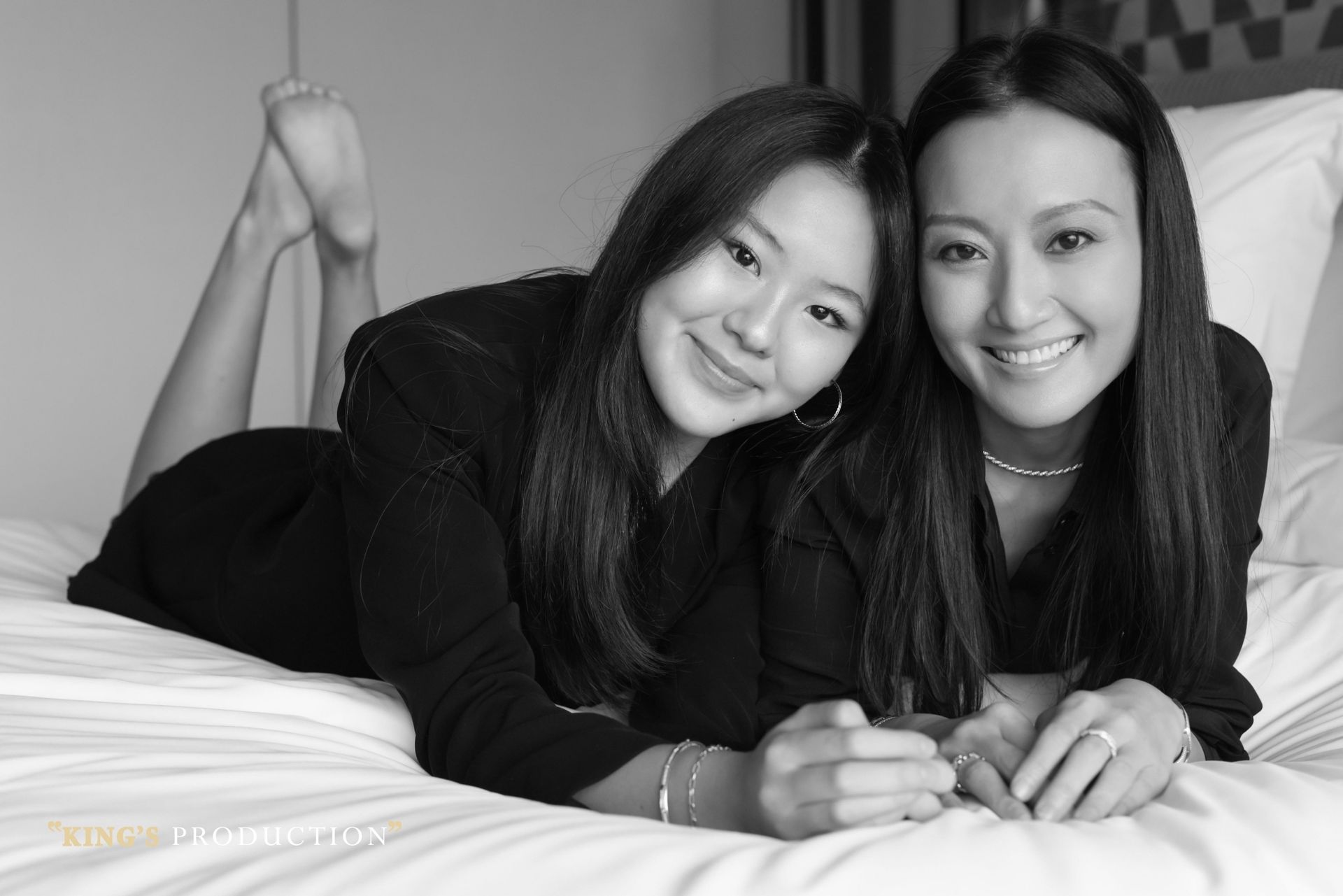 兩名微笑的女子躺在床上，其中一人抬起腳，黑白照片。