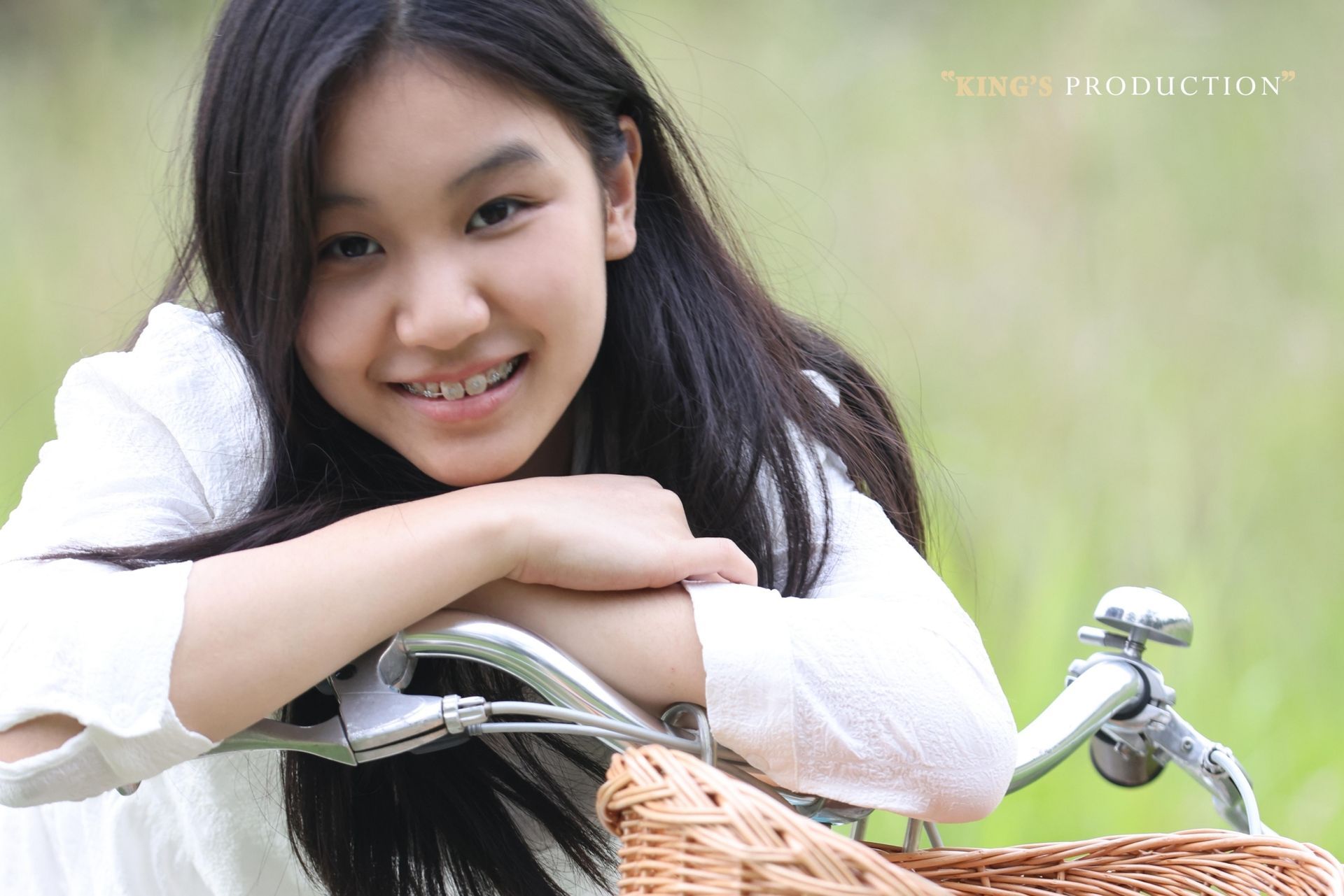田野裡，戴著牙套的亞洲小女孩靠在腳踏車車把上微笑。