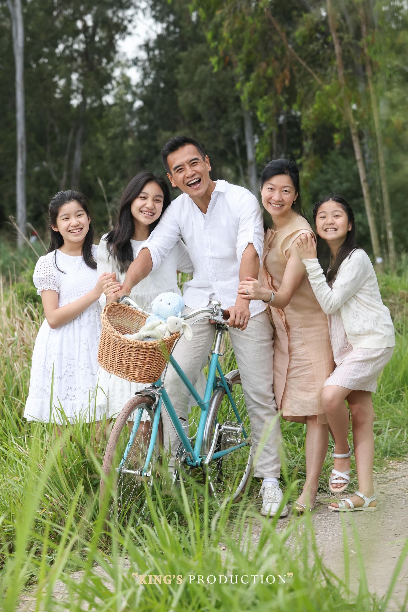 一家五口面帶微笑，聚集在戶外草地上的一輛綠松石自行車旁。
