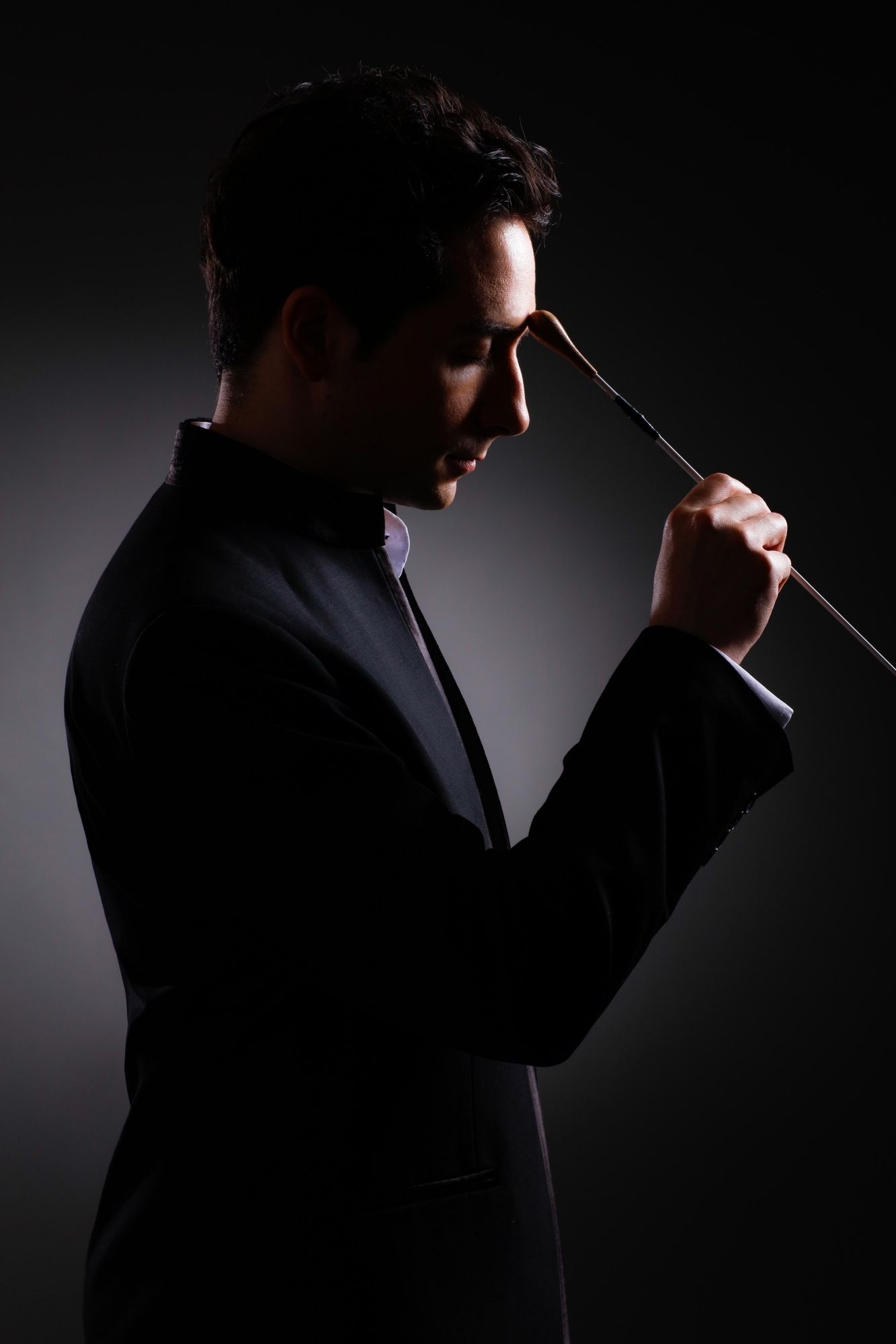 身穿西裝的男子，在黑暗的背景下，將指揮棒放在頭上思考。