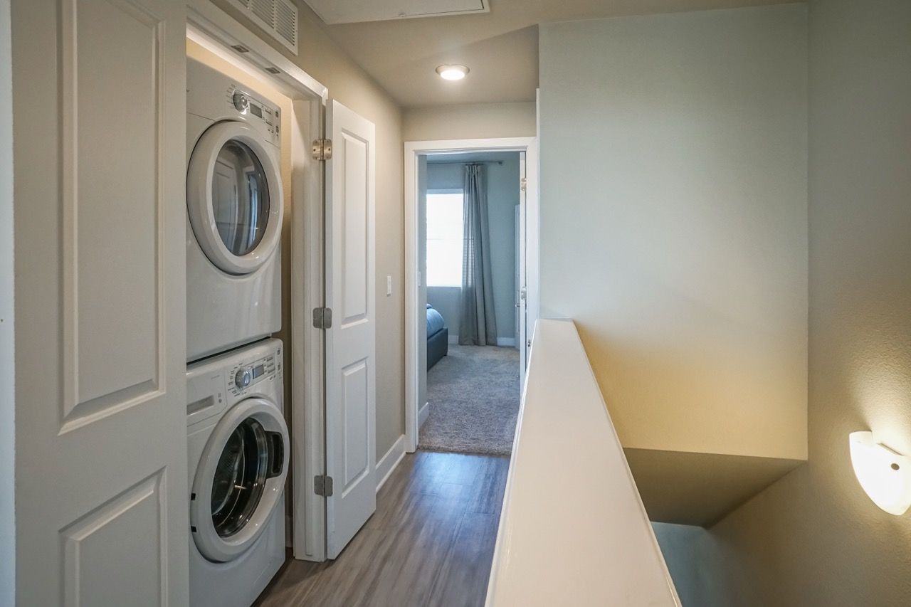 Stacked washer and dryer in a closet along a hallway near the stairwell.