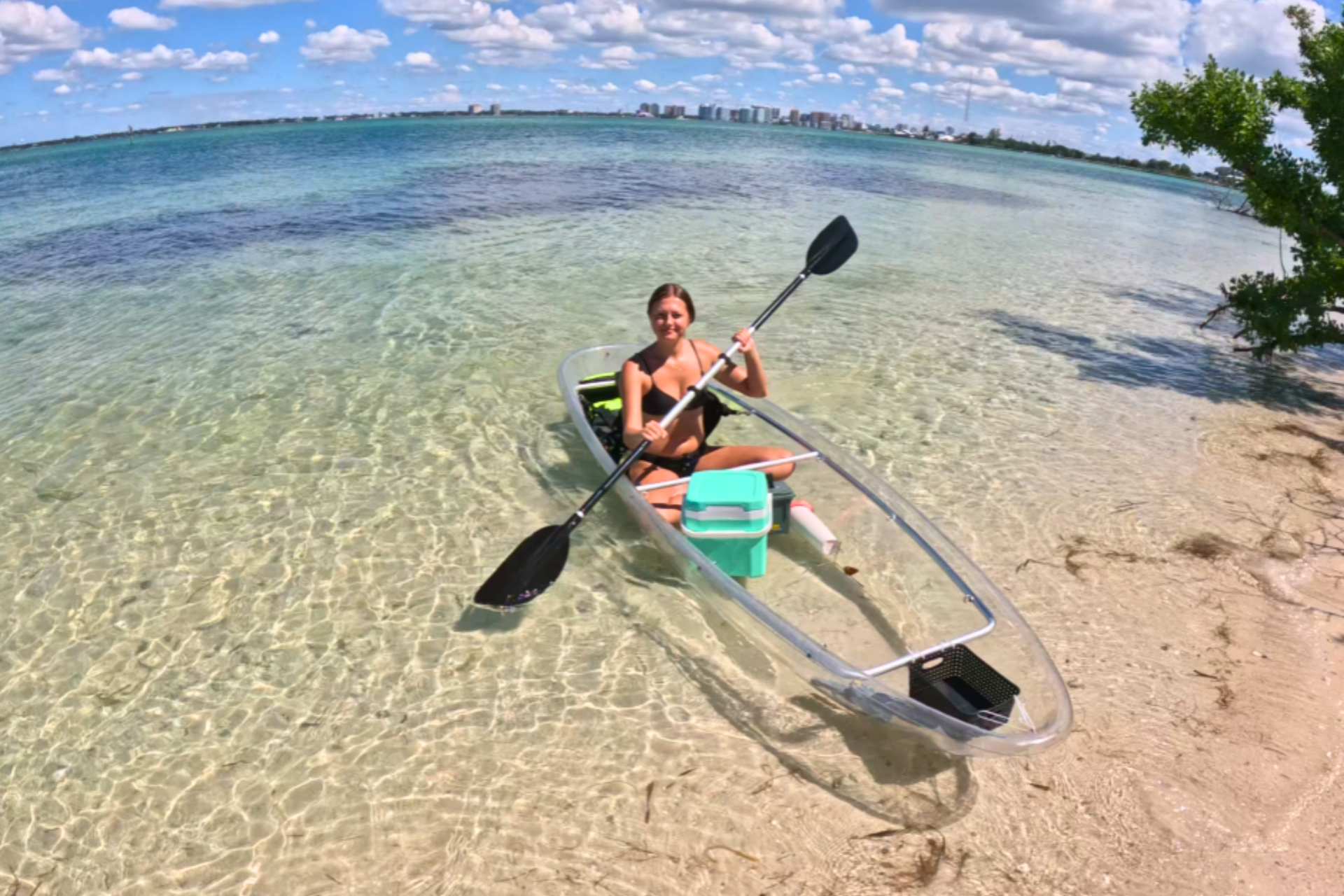 Girl in a transparent kayak paddling through calm, clear waters by the shore