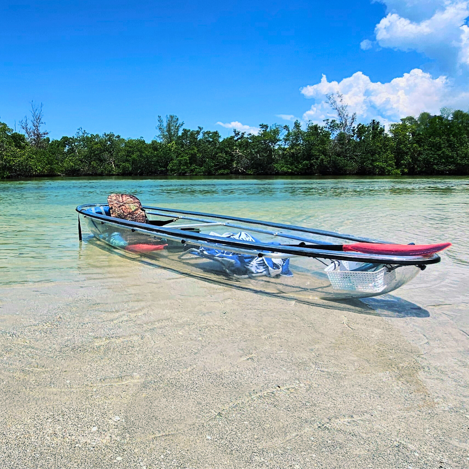 All clear kayak sitting in blue water on a sandbar.