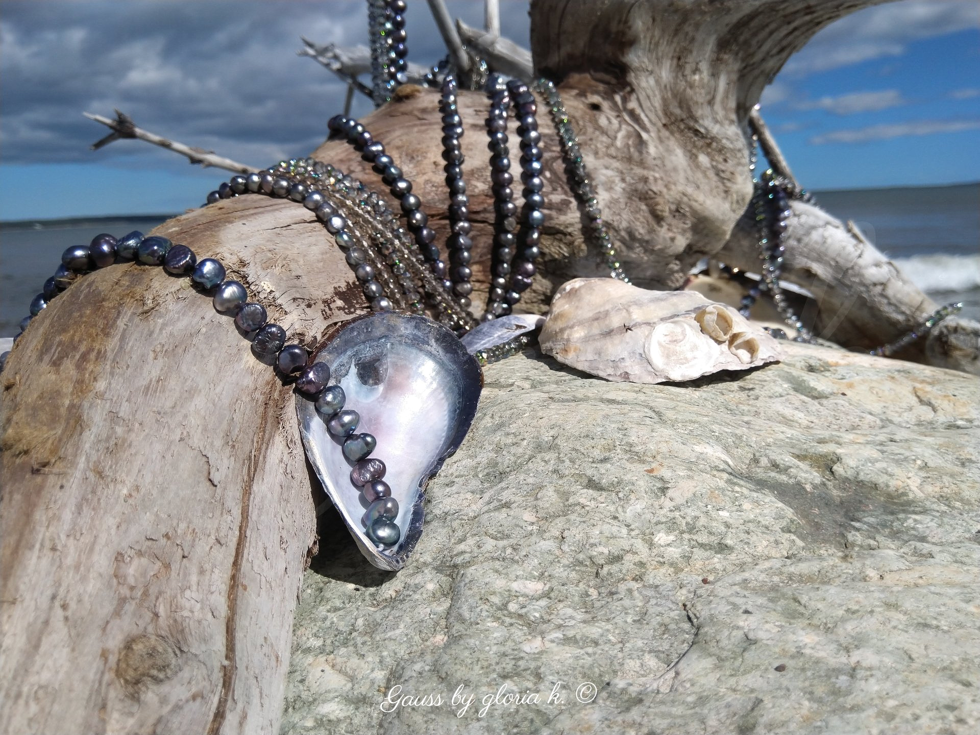 Driftwood sea creature draped with peacock pearls and crystals, close up.