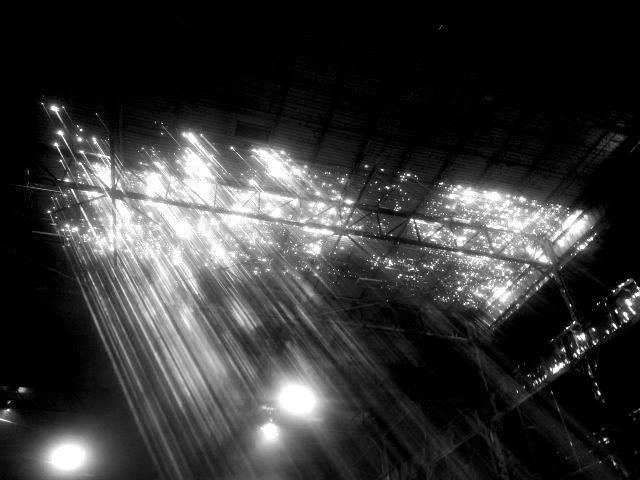 Black and white shot of sunlight streaming through a roof structure, illuminating a dark space.
