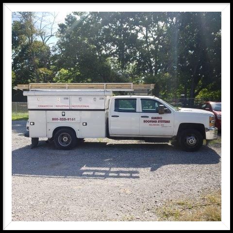 White work truck with a storage bed parked on gravel.