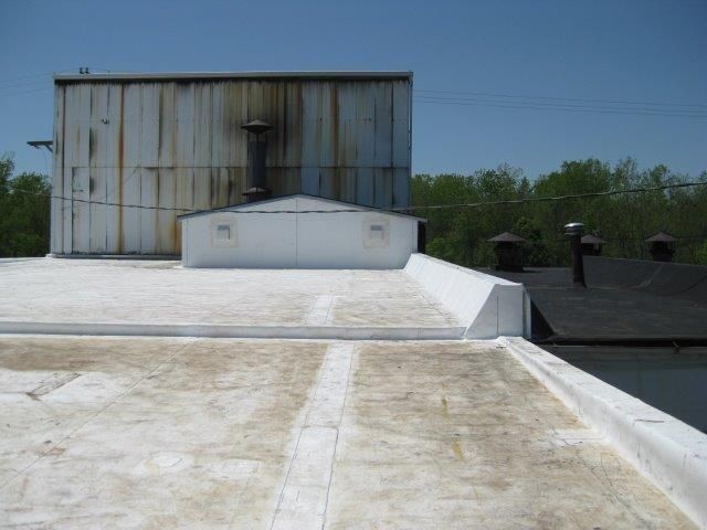 White flat roof with metal building, chimney, and trees in the background.