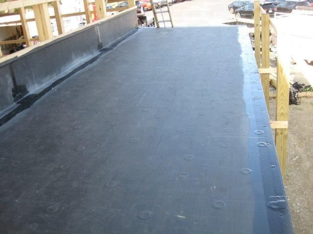 Black flat roof, wooden safety rails, partially constructed building in daylight.
