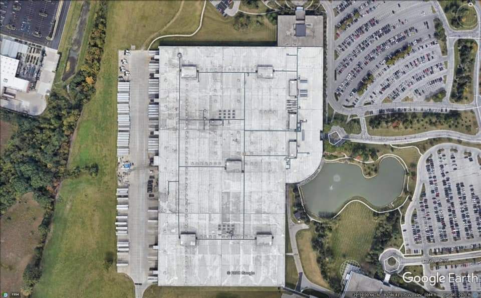 Aerial view of a large industrial building with loading docks, parking areas, and a pond.