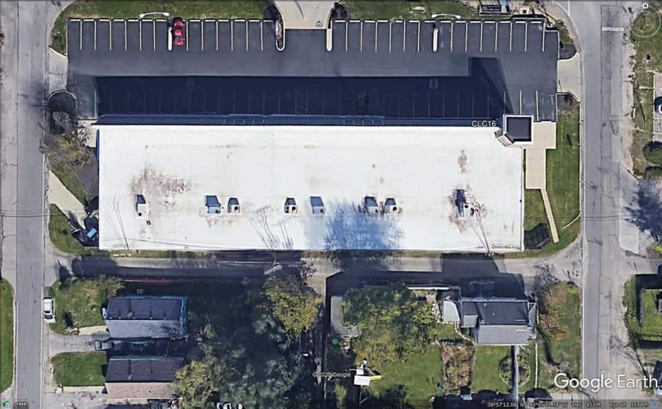 Overhead view of a white-roofed commercial building with a parking lot and surrounding houses on a suburban street.
