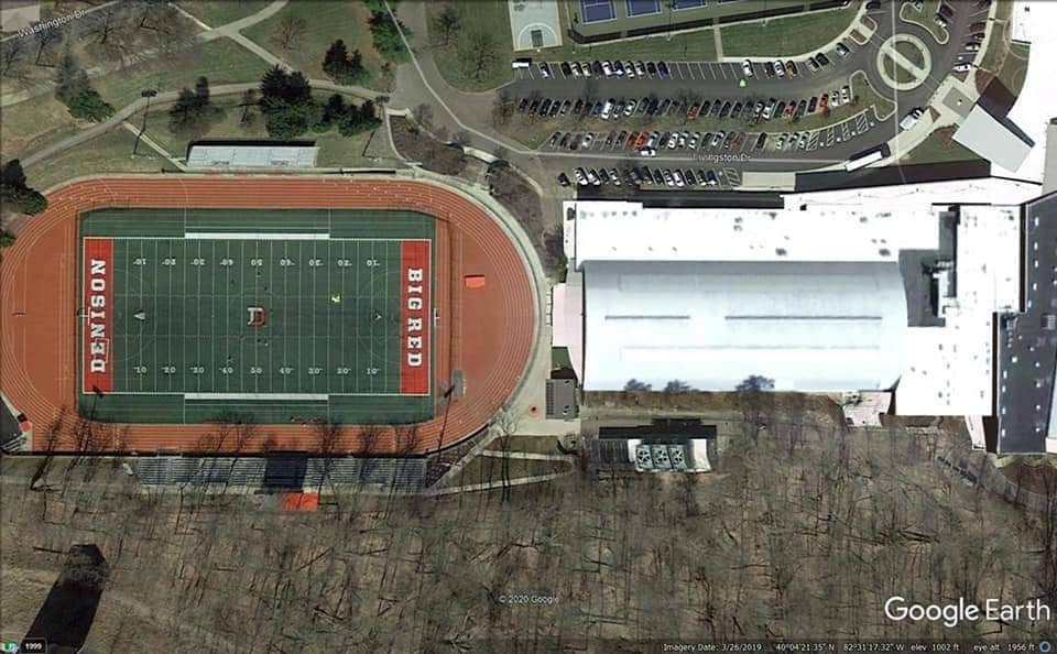 Aerial view of a football field with a track, and a large white building;