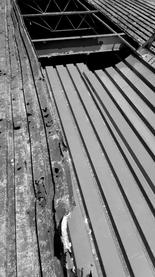 Black and white view of a damaged metal roof with a large opening exposing the interior structure.