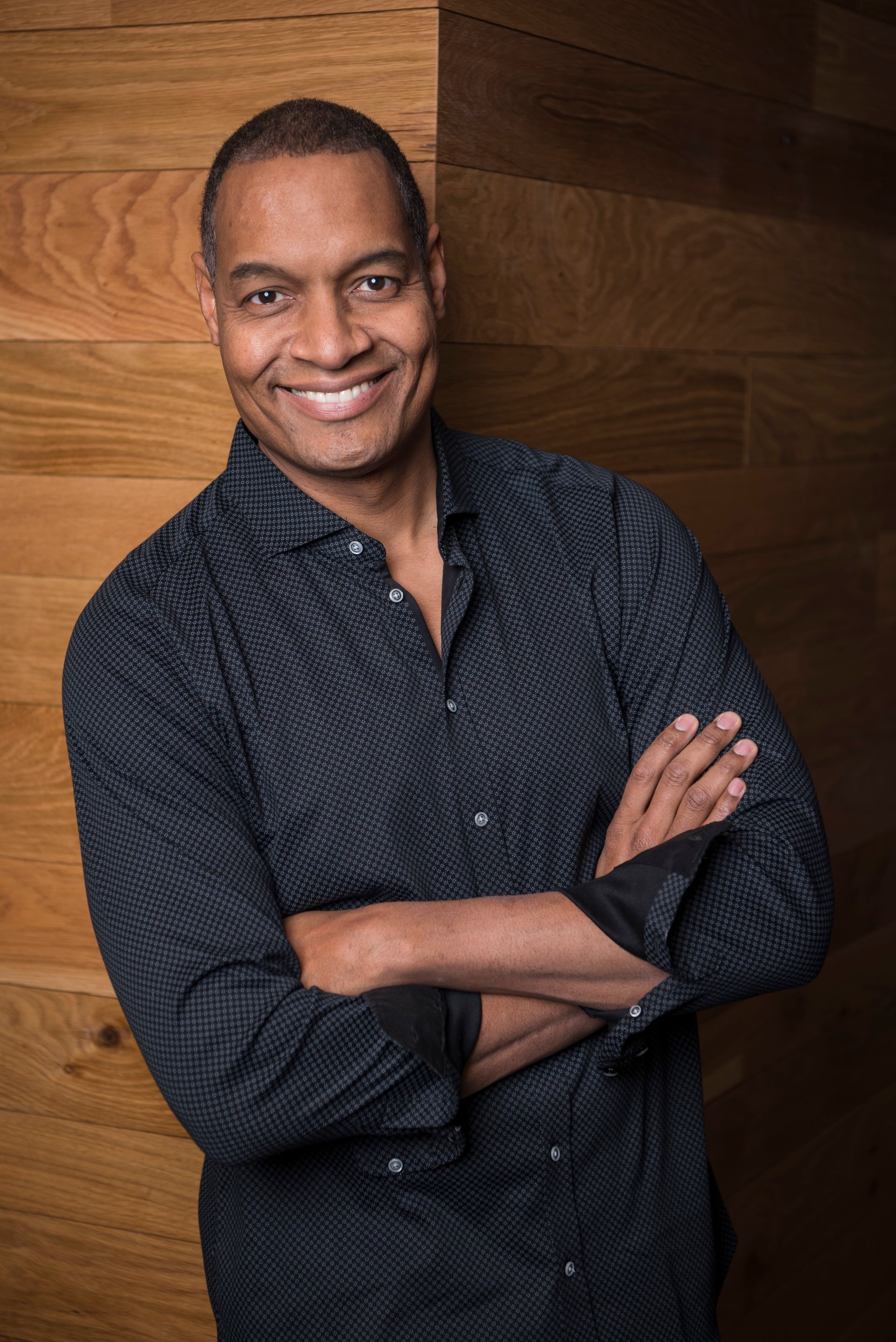 A man in a black shirt is smiling with his arms crossed