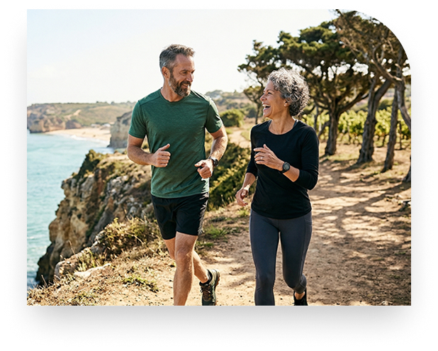 An active senior couple jogging together on a coastal trail.