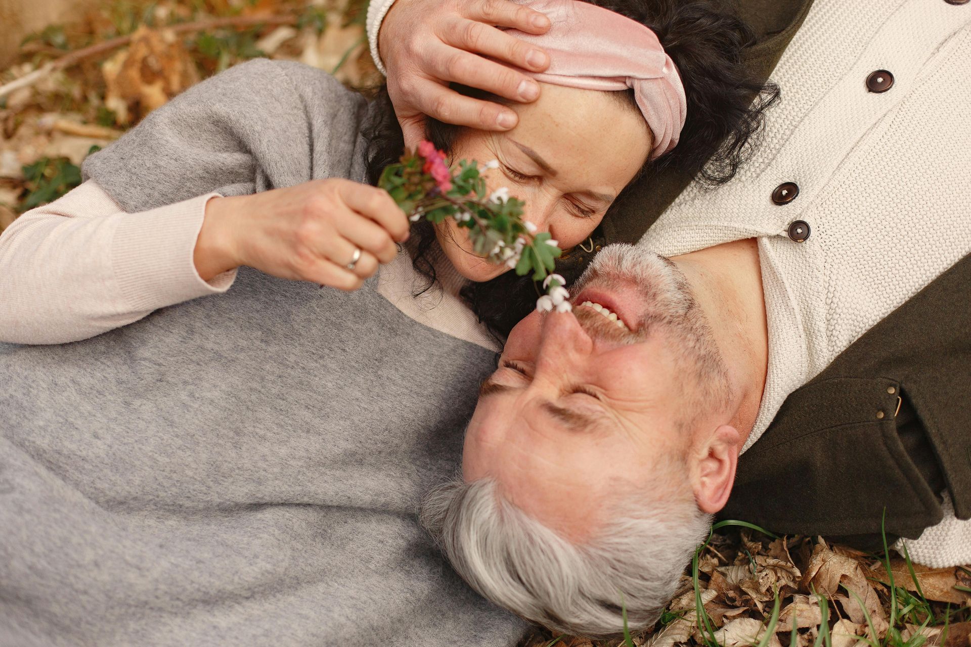 Couple lying outdoors, smiling, smelling flowers.