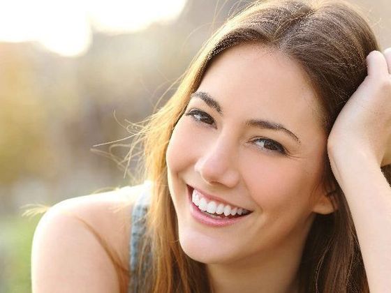 A close up of a woman smiling with her hand on her head.
