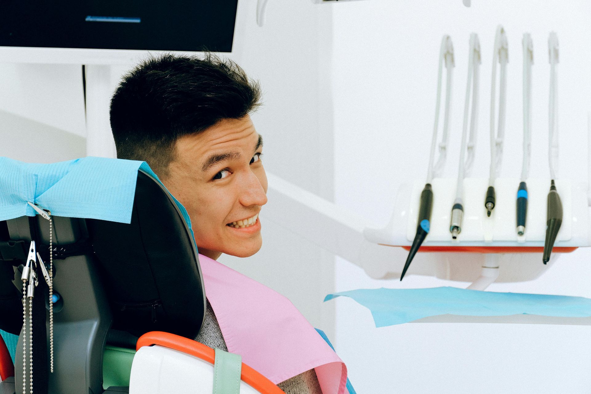 Person in a dentist chair smiles at the camera, tools visible in background.