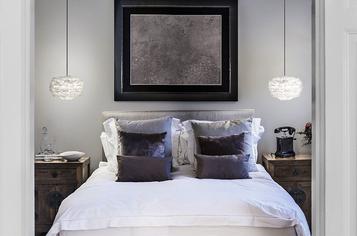 A bedroom with a bed , nightstands , lamps and a picture on the wall.