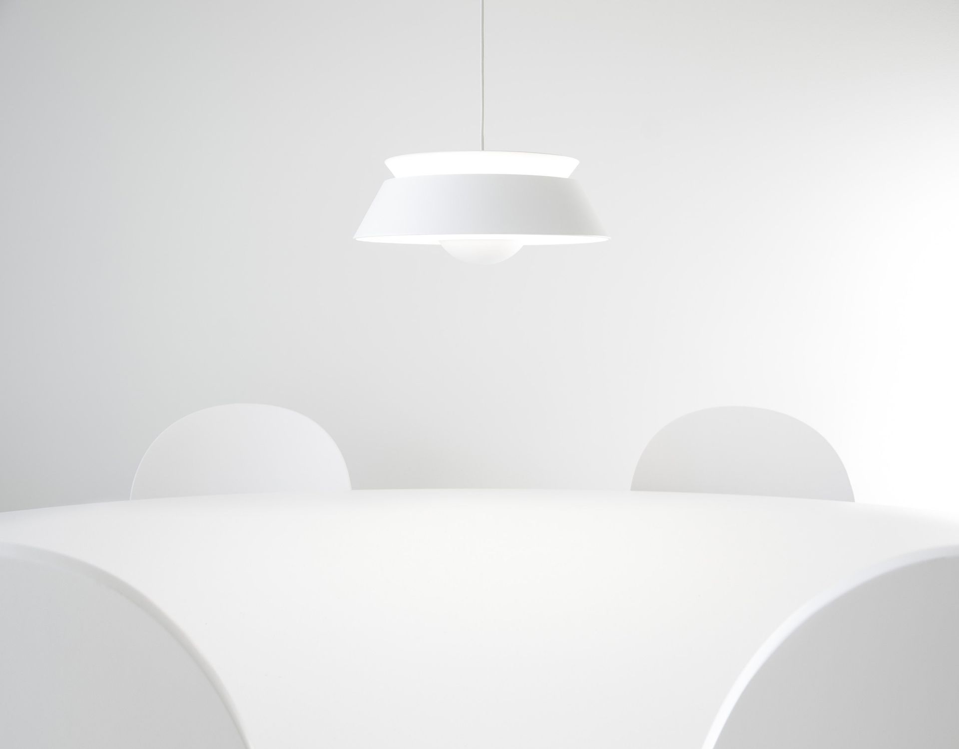 A white table and chairs in a room with a white lamp hanging from the ceiling.