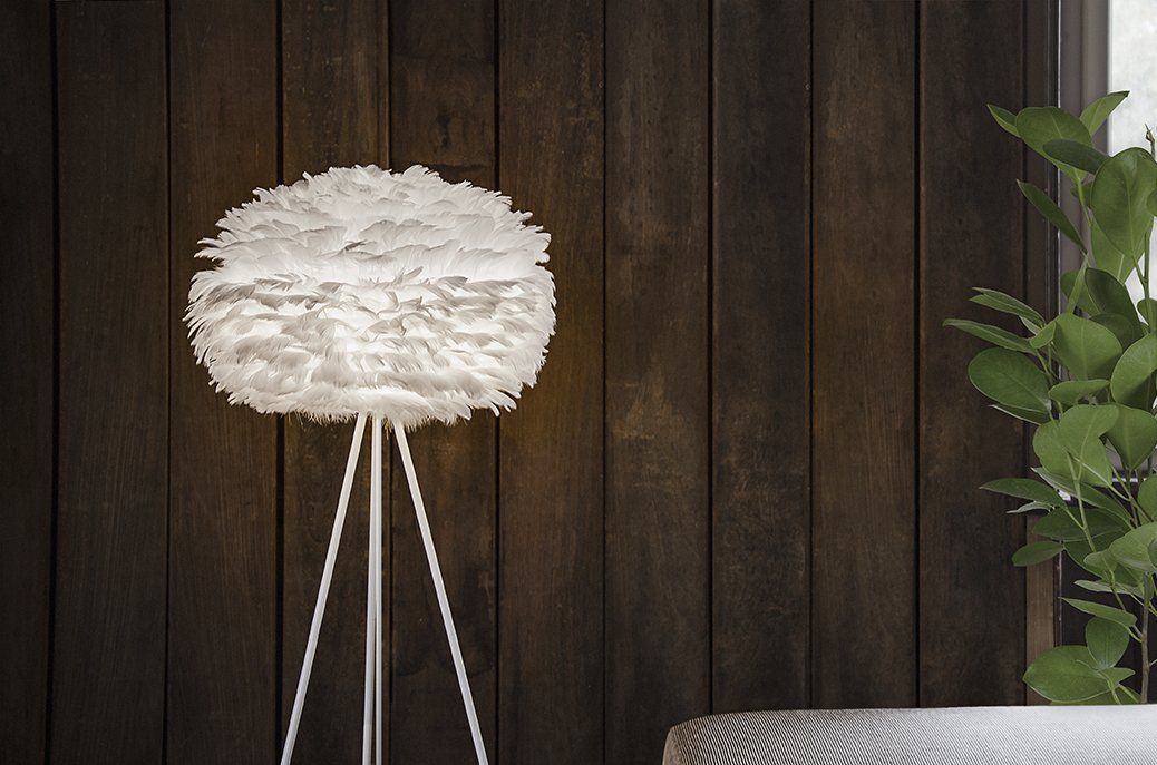 A white feather lamp is sitting on a tripod in front of a wooden wall.
