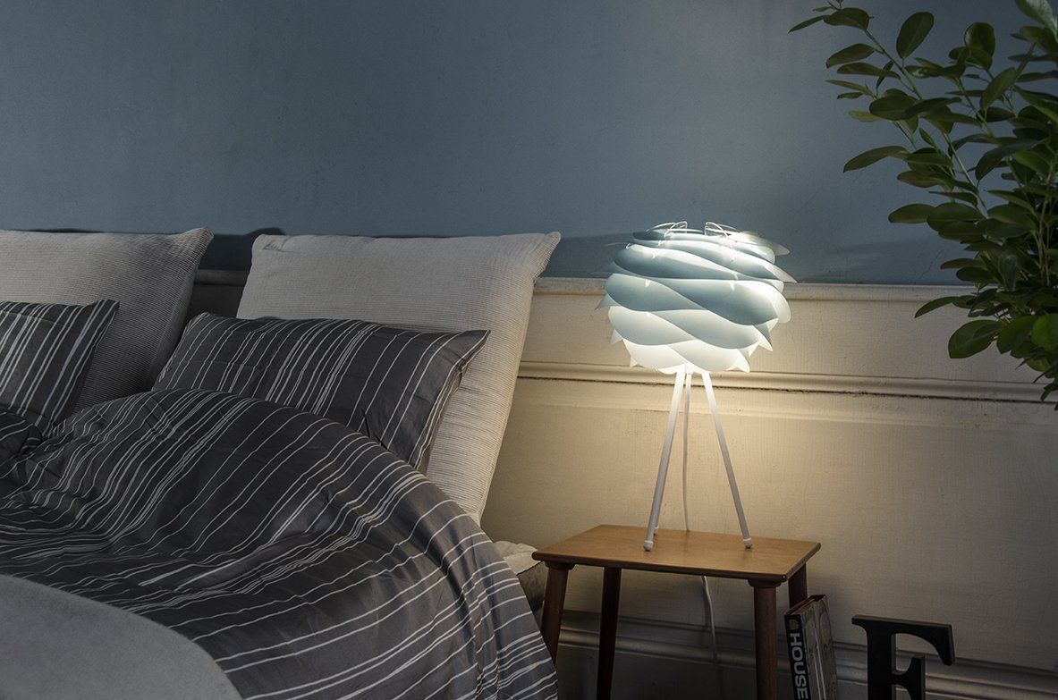 A bedroom with a bed and a table with a lamp on it.