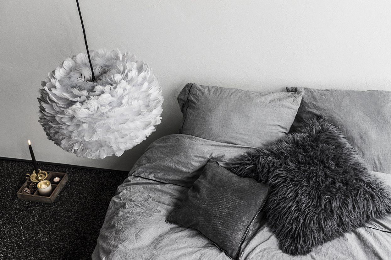 A black and white photo of a bed with a lamp hanging from the ceiling.