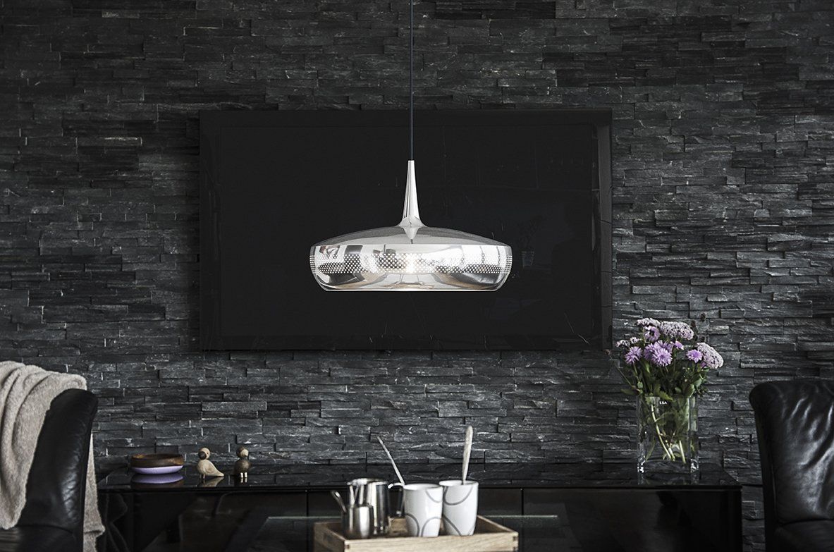 A living room with a black brick wall and a silver pendant light hanging from the ceiling.